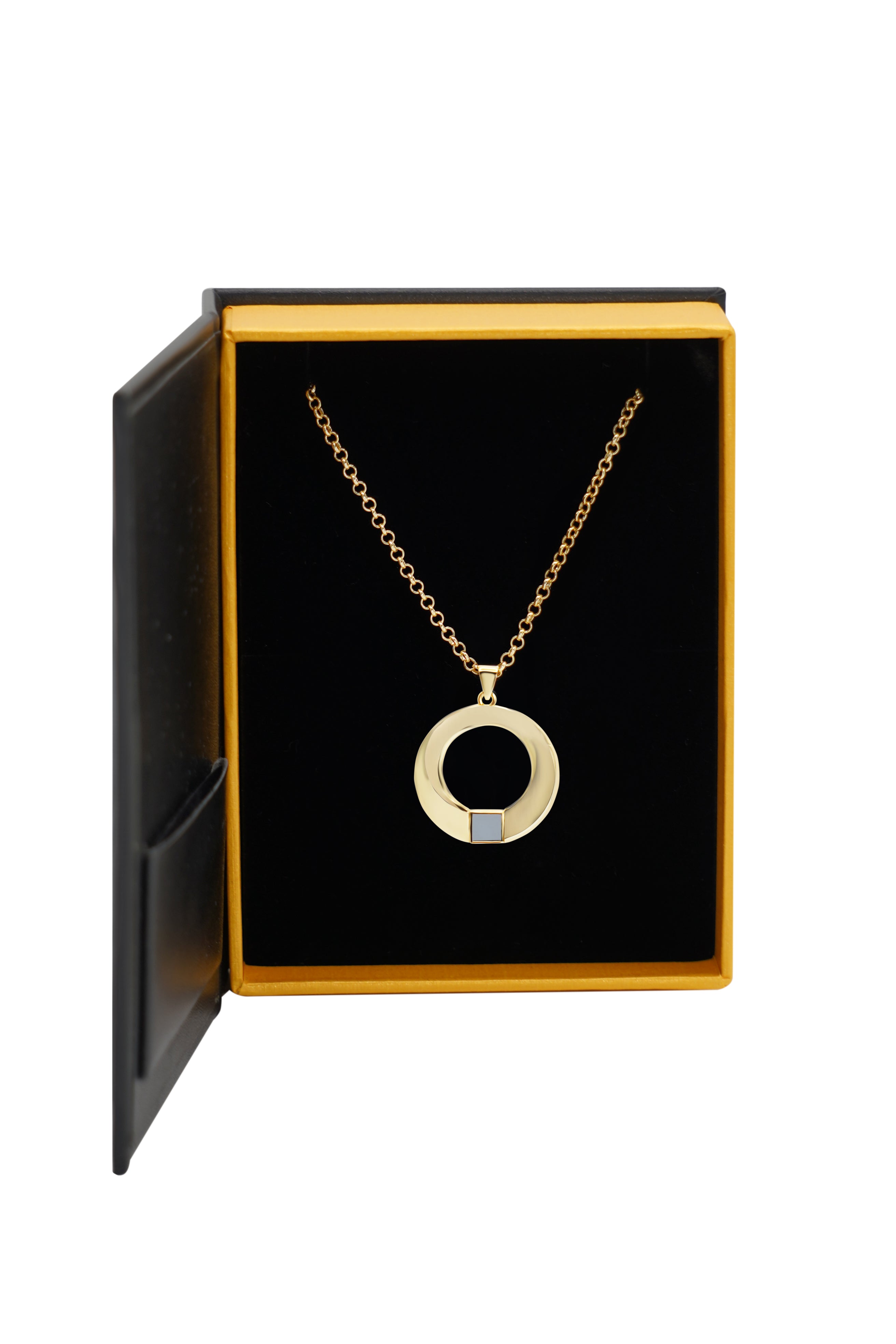 The Eternity Circle Necklace—a gold circular pendant with a cut-out center and a small rectangular accent—comes elegantly displayed in an open black and gold jewelry box.