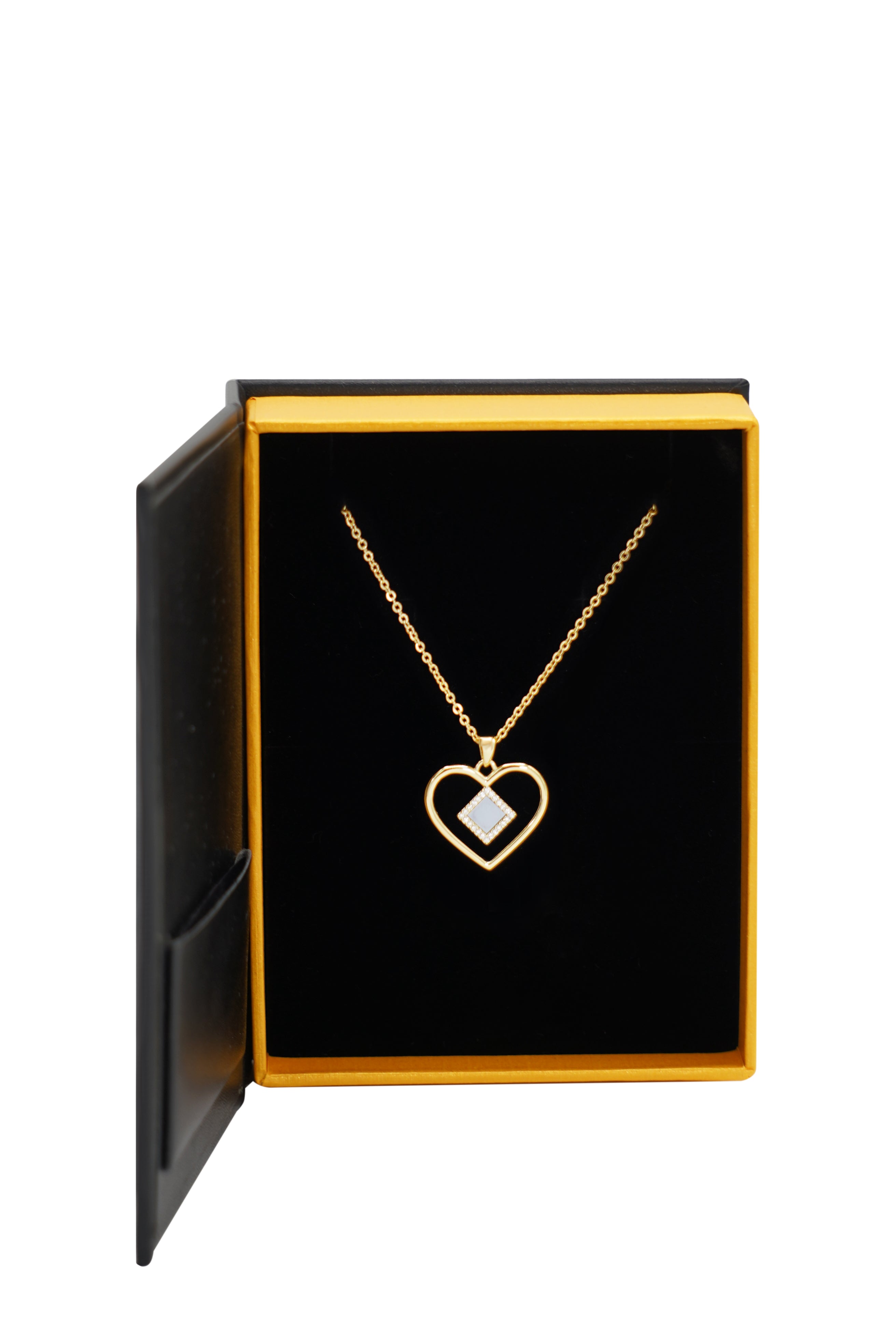 The Heart Necklace | Old Testament Edition by Nano Jewelry features a gold heart-shaped pendant with a small square gem, presented in an open black and gold jewelry box.