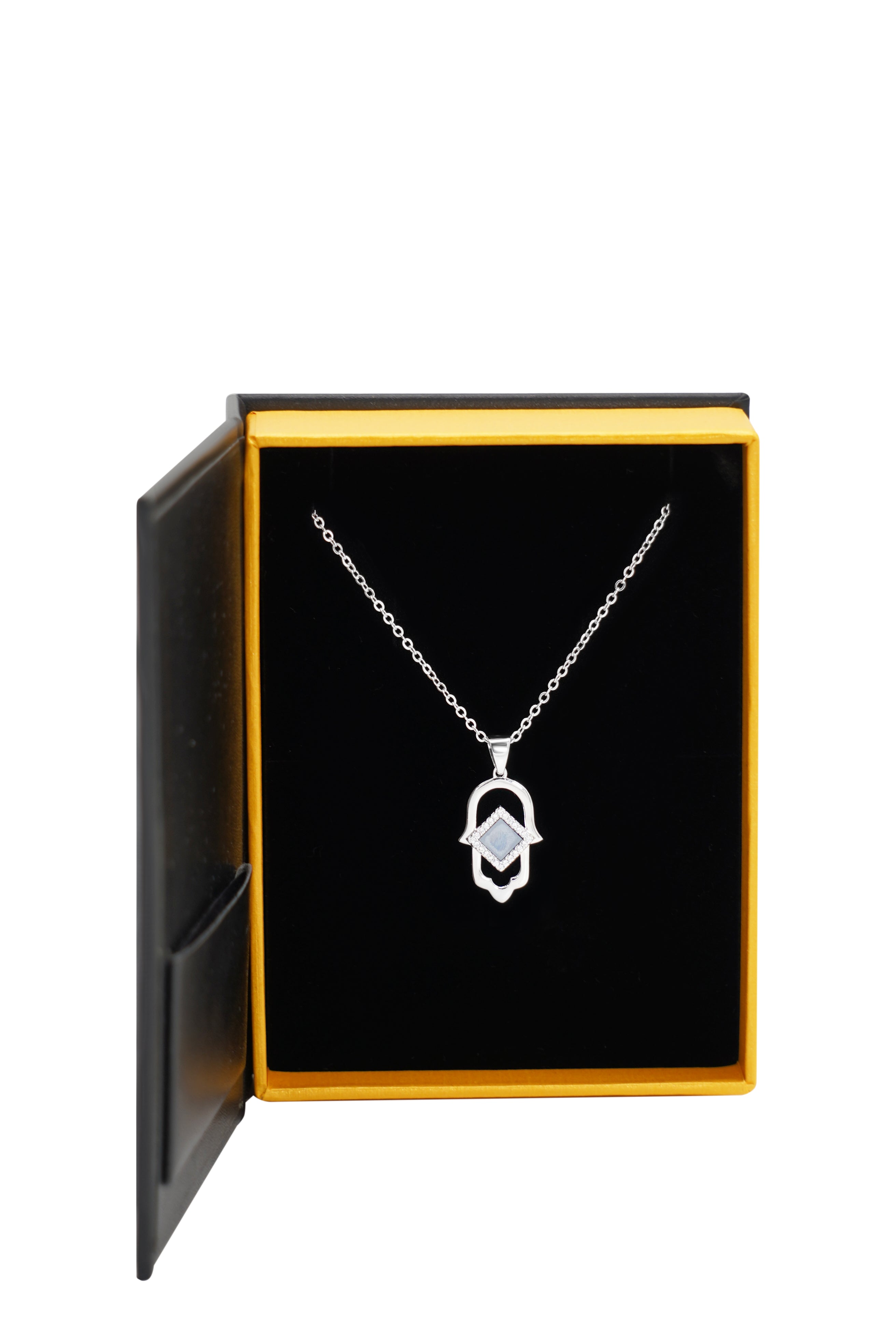 The Hamsa Necklace | Old Testament Edition—a silver geometric pendant inspired by Christian jewelry—comes displayed in an open black and yellow jewelry box with a soft black interior.