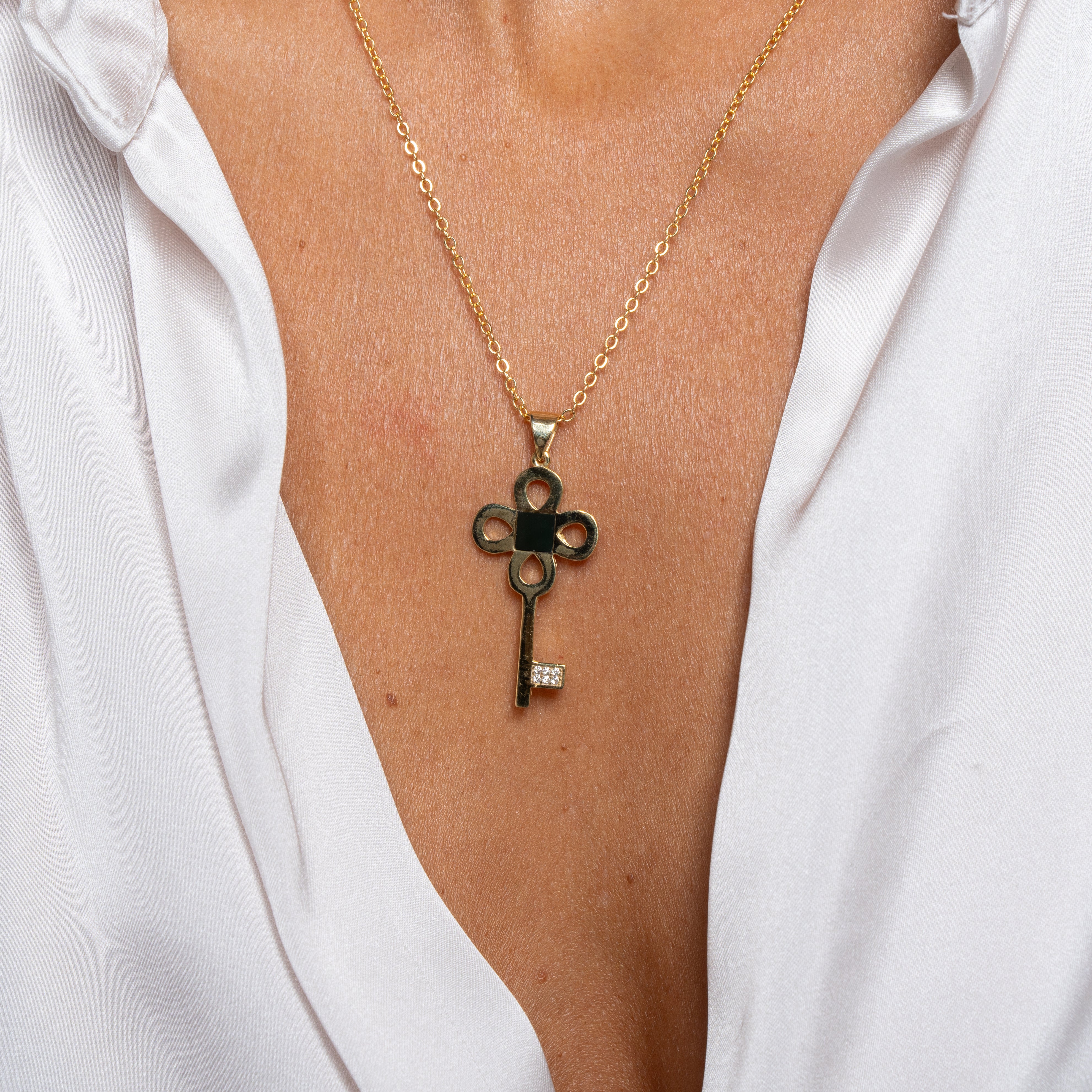 The Key Necklace - Old Testament Edition, a gold key-shaped pendant inspired by Jewish jewelry, rests on a persons chest as they wear a white, partially open shirt.