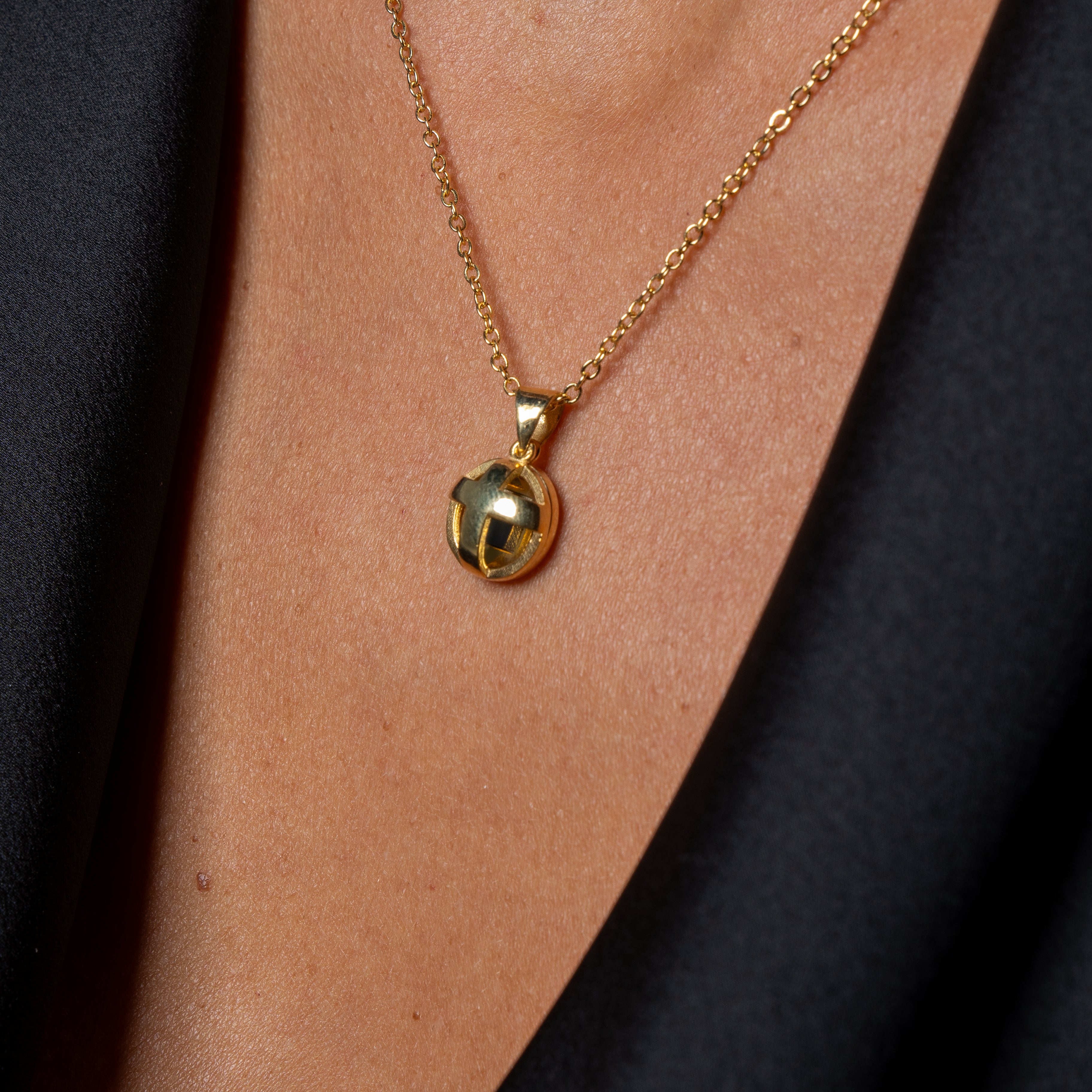 A close-up of a person wearing the Opening Cross gold pendant necklace with a round charm, showcasing elegant Jewish jewelry against their bare chest, dressed in a black deep V-neck garment.