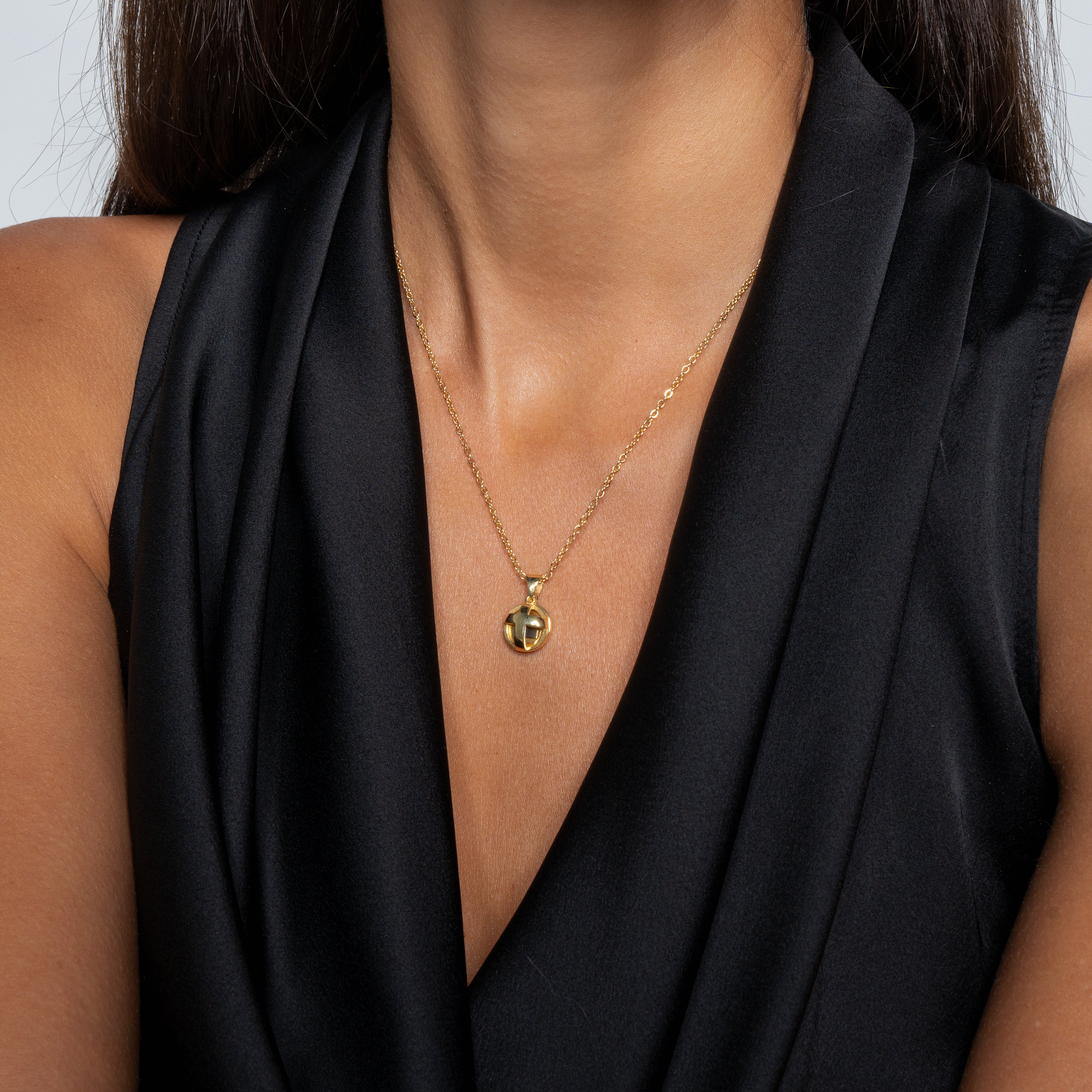A woman wears a sleeveless black dress with a gold Nano Jewelry pendant necklace featuring the Opening Cross design, shown from shoulders to chin against a plain background.