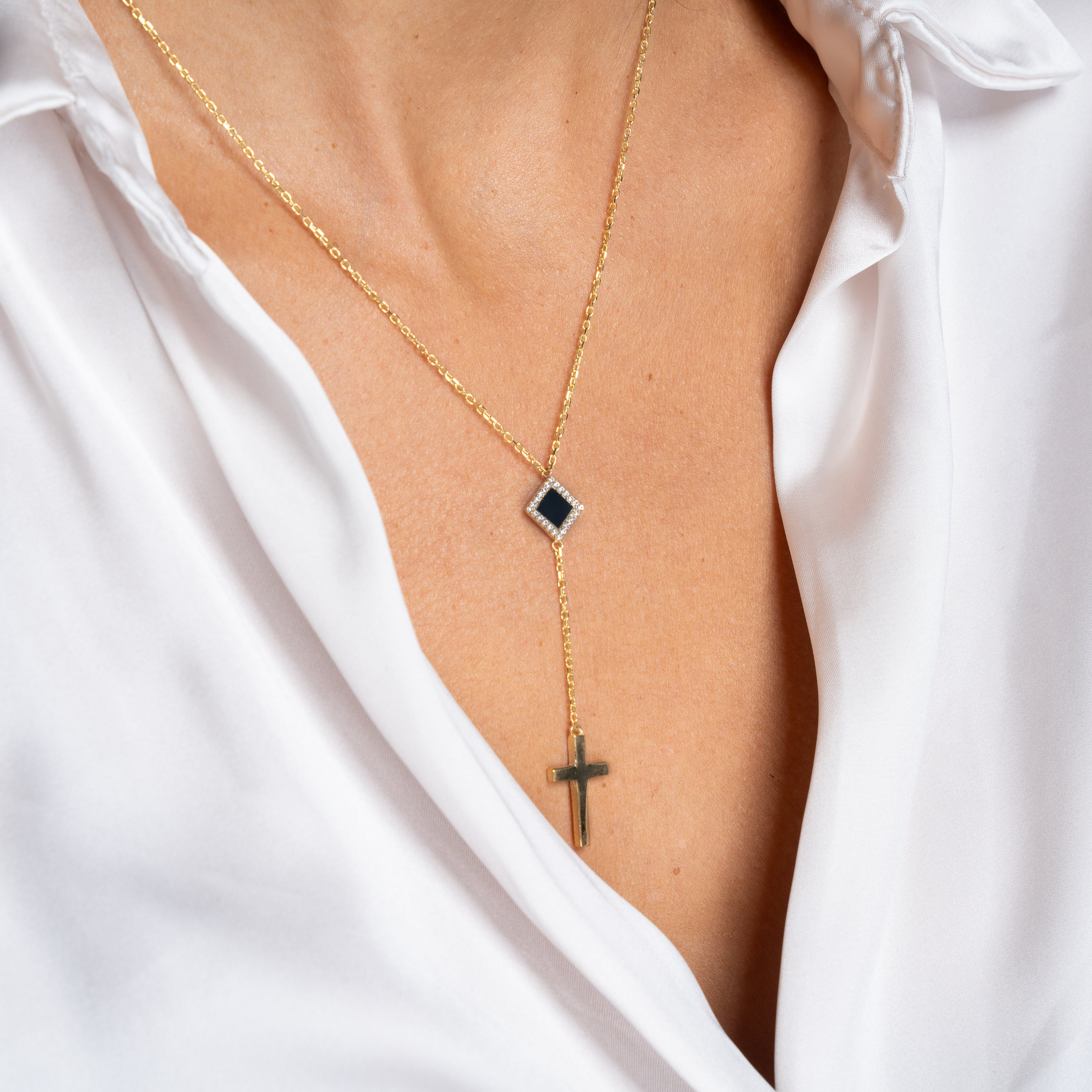 The Mini Cross Y Necklace features a black gemstone pendant and hanging gold cross, elegantly worn over bare skin and partially visible inside a white, open-collared shirt—a stunning piece of Christian jewelry.